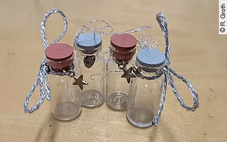 Alte Impffläschchen wurden mit einer Schleife und einem kleinen Anhänger zu einem Andenken für die Besitzer*innen umfunktioniert.
