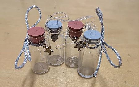 Alte Impffläschchen wurden mit einer Schleife und einem kleinen Anhänger zu einem Andenken für die Besitzer*innen umfunktioniert.