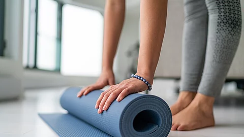 Yoga at home woman rolling exercise mat in living room of house or apartment condo for morning wellness yoga practice.