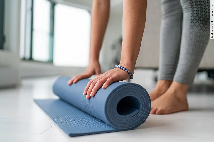 Yoga at home woman rolling exercise mat in living room of house or apartment condo for morning wellness yoga practice.