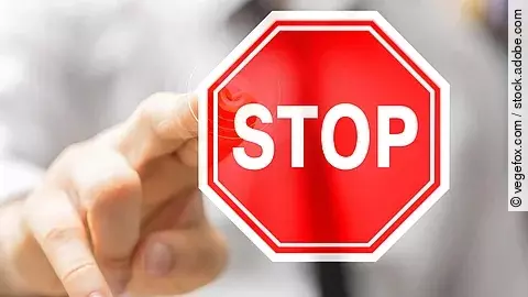 Eine Person in weißem Hemd und dunkler Krawatte zeigt mit seiner Hand auf ein Stop-Schild. 