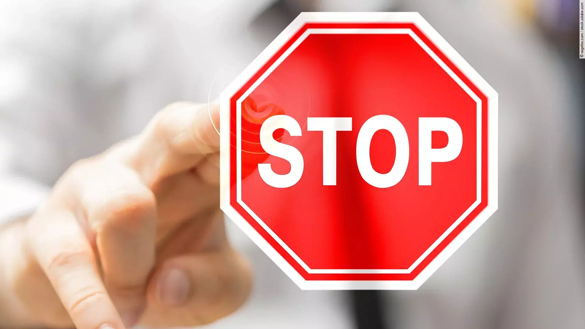 Eine Person in weißem Hemd und dunkler Krawatte zeigt mit seiner Hand auf ein Stop-Schild. 