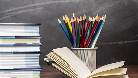 Ein aufgeschlagenes Buch liegt neben weiteren Büchern und Stiften auf einem Schreibtisch.