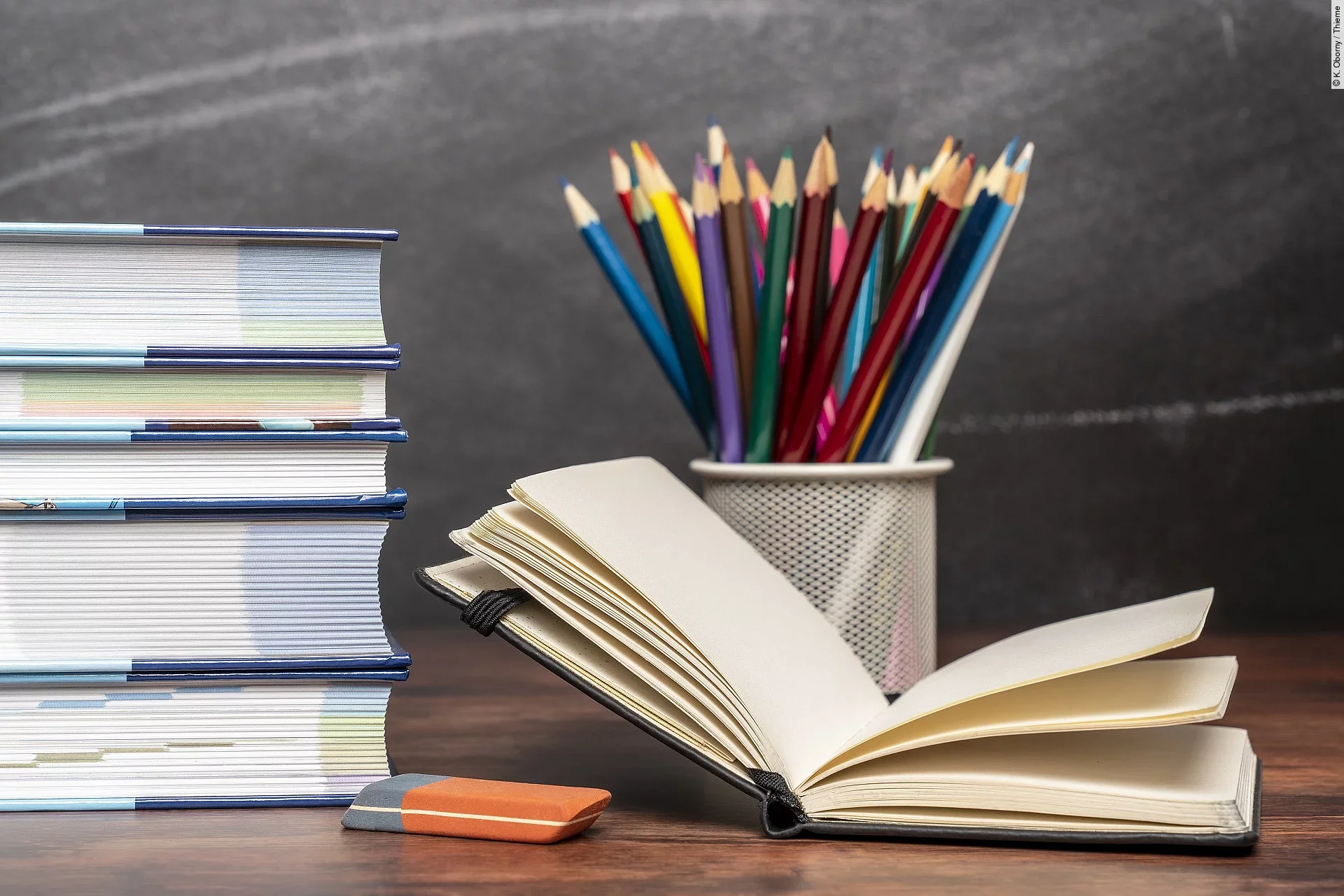 Ein aufgeschlagenes Buch liegt neben weiteren Büchern und Stiften auf einem Schreibtisch.