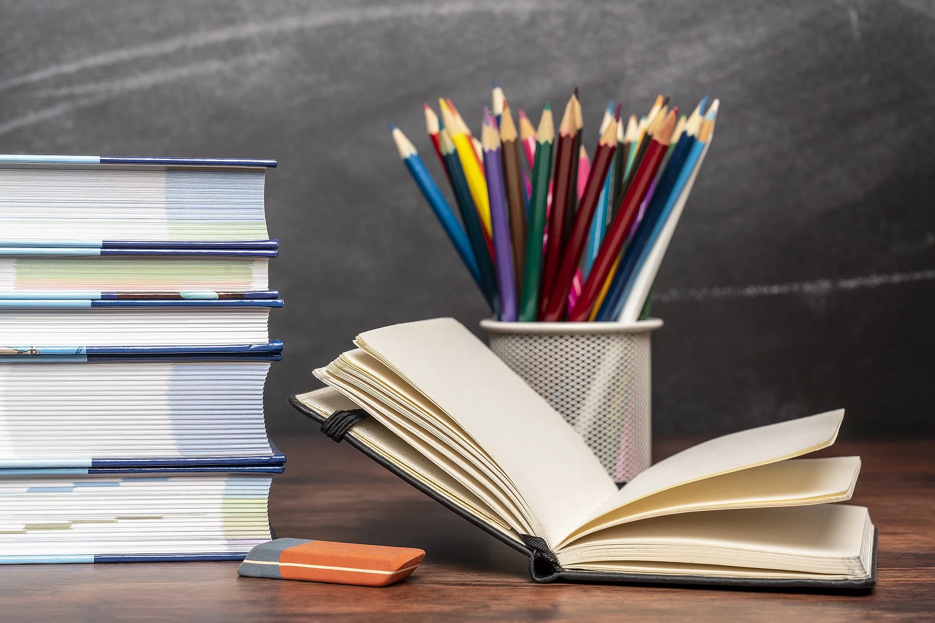Ein aufgeschlagenes Buch liegt neben weiteren Büchern und Stiften auf einem Schreibtisch.