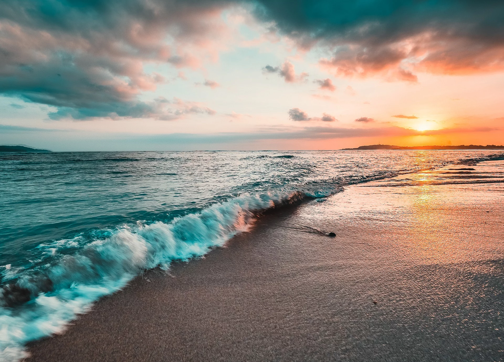 Das Meer von der Küste aus fotografiert. Im Hintergrund sieht man einen bunten Himmel durch die Sonne.