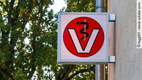 Ein Schild an einer Tierarztpraxis zeigt eine schwarze Schlange, die sich um einen weißen Stab wickelt in einem großen V wickelt.