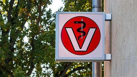 Ein Schild an einer Tierarztpraxis zeigt eine schwarze Schlange, die sich um einen weißen Stab wickelt in einem großen V wickelt. Ein Schild an einer Tierarztpraxis zeigt eine schwarze Schlange, die sich um einen weißen Stab wickelt in einem großen V wickelt.