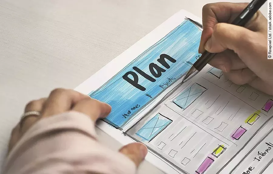 Ein Planzettel liegt im Fokus des Bildes, darauf schreibt eine Person mit Stift..