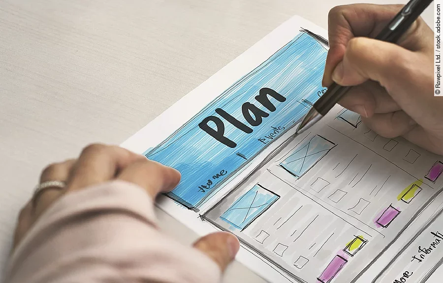 Ein Planzettel liegt im Fokus des Bildes, darauf schreibt eine Person mit Stift..