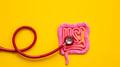 Auf gelben Hintergrund liegt ein rosa Darm aus Knete. Dabei hört ein rotes Stethoskop den Darm ab.