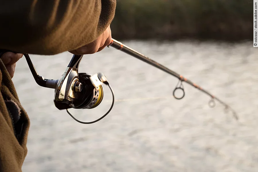 Nahaufnahme von einer Person mit einer Angelrute die an einem Fluss steht und fischt.
