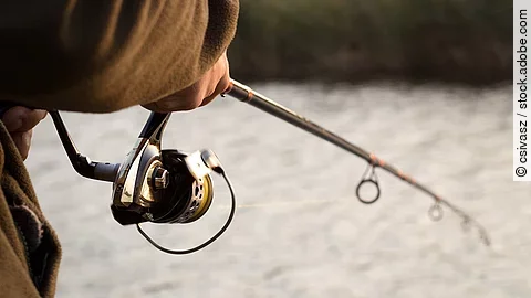 Nahaufnahme von einer Person mit einer Angelrute die an einem Fluss steht und fischt.