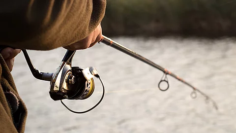 Nahaufnahme von einer Person mit einer Angelrute die an einem Fluss steht und fischt.