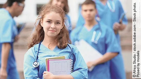 Eine Medizin-Studierende Person hält einen Block in den Armen und schaut in die Kamera.