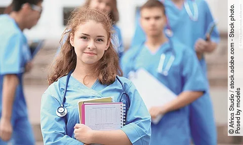 Eine Medizin-Studierende Person hält einen Block in den Armen und schaut in die Kamera.