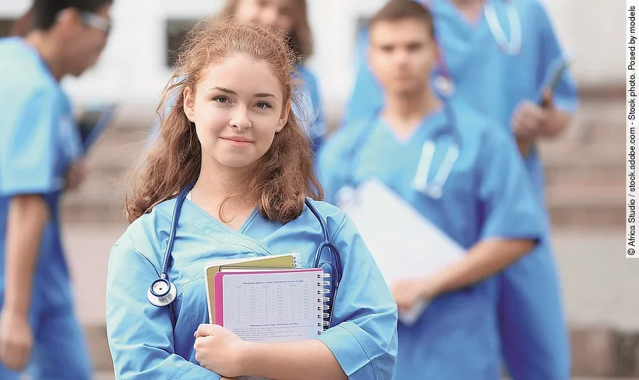 Eine Medizin-Studierende Person hält einen Block in den Armen und schaut in die Kamera.