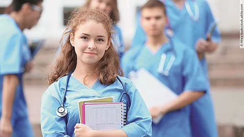 Eine Medizin-Studierende Person hält einen Block in den Armen und schaut in die Kamera.