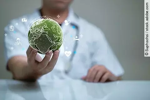 Ein Arzt in weißem Kassack hält eine grüne, moosbewachsene Weltkugel in der Hand.