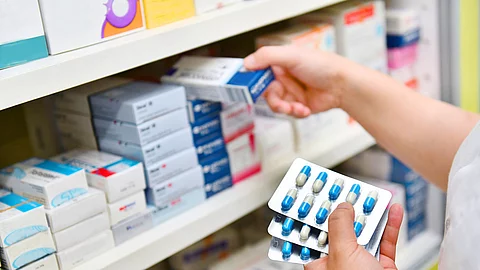 Ein Apotheker räumt Arzneimittel in ein Regal ein. Dabei hält er mehrere Tablettenblister in der einen Hand und eine Arzneimittelpackung in der anderen. Ein Apotheker räumt Arzneimittel in ein Regal ein. Dabei hält er mehrere Tablettenblister in der einen Hand und eine Arzneimittelpackung in der anderen.