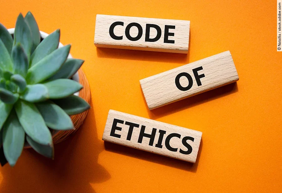 Auf einem orangenen Boden liegen 3 Holzklötze mit der Aufschrift Code of Ethics. Im linken Teil des Bildes steht eine Pflanze. Auf einem orangenen Boden liegen 3 Holzklötze mit der Aufschrift Code of Ethics. Im linken Teil des Bildes steht eine Pflanze.