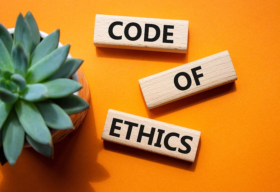 Auf einem orangenen Boden liegen 3 Holzklötze mit der Aufschrift Code of Ethics. Im linken Teil des Bildes steht eine Pflanze. Auf einem orangenen Boden liegen 3 Holzklötze mit der Aufschrift Code of Ethics. Im linken Teil des Bildes steht eine Pflanze.