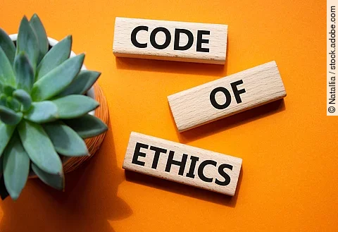 Auf einem orangenen Boden liegen 3 Holzklötze mit der Aufschrift Code of Ethics. Im linken Teil des Bildes steht eine Pflanze.
