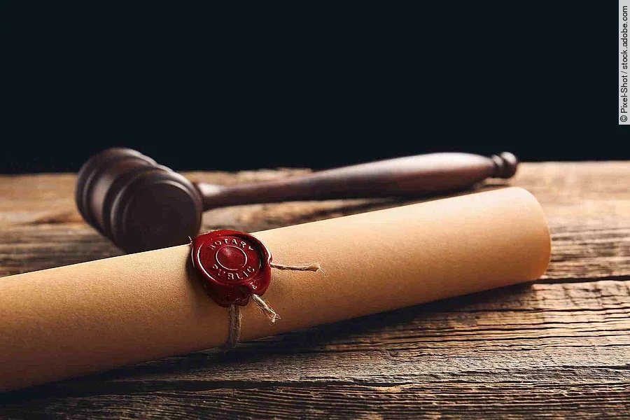 Eine Papierrolle mit rotem Siegel liegt auf einem Holztisch. Daneben liegt ein hölzerner Richterhammer. Eine Papierrolle mit rotem Siegel liegt auf einem Holztisch. Daneben liegt ein hölzerner Richterhammer.