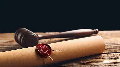 Eine Papierrolle mit rotem Siegel liegt auf einem Holztisch. Daneben liegt ein hölzerner Richterhammer. Eine Papierrolle mit rotem Siegel liegt auf einem Holztisch. Daneben liegt ein hölzerner Richterhammer.