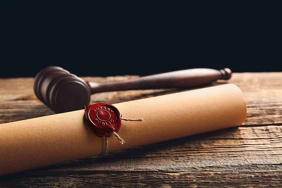 Eine Papierrolle mit rotem Siegel liegt auf einem Holztisch. Daneben liegt ein hölzerner Richterhammer.