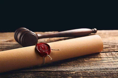 Eine Papierrolle mit rotem Siegel liegt auf einem Holztisch. Daneben liegt ein hölzerner Richterhammer.