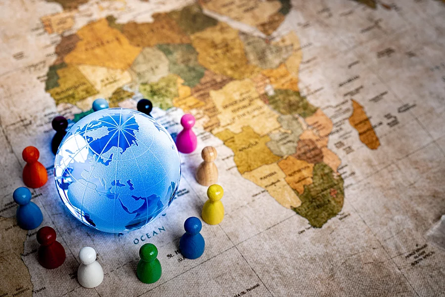 Auf einer alten Weltkarte sieht man den Afrikanischen Kontinent. In der unteren linken Ecke ist zudem noch ein blau leuchtender Globus um den bunte Spielfiguren stehen.