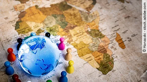 Auf einer alten Weltkarte sieht man den Afrikanischen Kontinent. In der unteren linken Ecke ist zudem noch ein blau leuchtender Globus um den bunte Spielfiguren stehen.