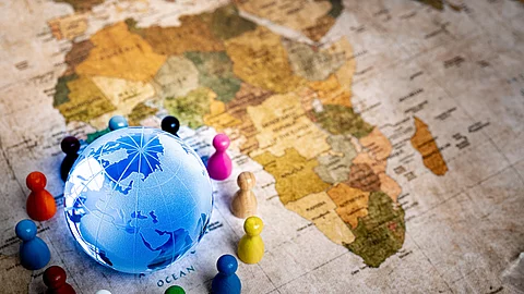 Auf einer alten Weltkarte sieht man den Afrikanischen Kontinent. In der unteren linken Ecke ist zudem noch ein blau leuchtender Globus um den bunte Spielfiguren stehen.