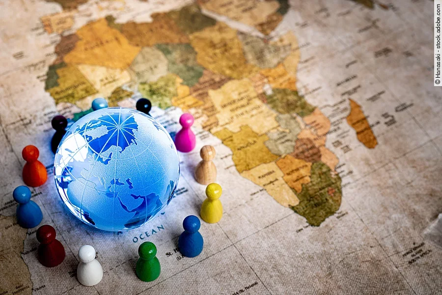 Auf einer alten Weltkarte sieht man den Afrikanischen Kontinent. In der unteren linken Ecke ist zudem noch ein blau leuchtender Globus um den bunte Spielfiguren stehen.