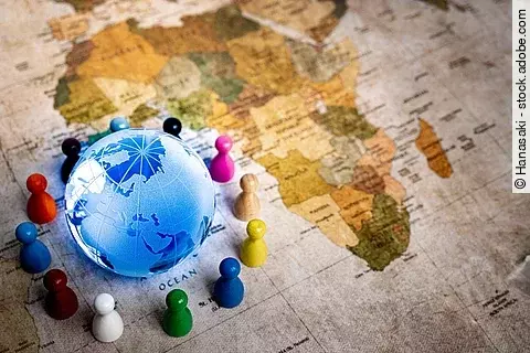 Auf einer alten Weltkarte sieht man den Afrikanischen Kontinent. In der unteren linken Ecke ist zudem noch ein blau leuchtender Globus um den bunte Spielfiguren stehen.