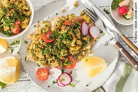 Aufnahme von einem knusprigen Toastbrot mit Rührei aus Tofu und Tomatensalat. Über dem Tofu ist Schnittlauch gestreut. Das Essen ist auf einem Teller angerichtet und daneben liegen ein Set Messer und Gabel.