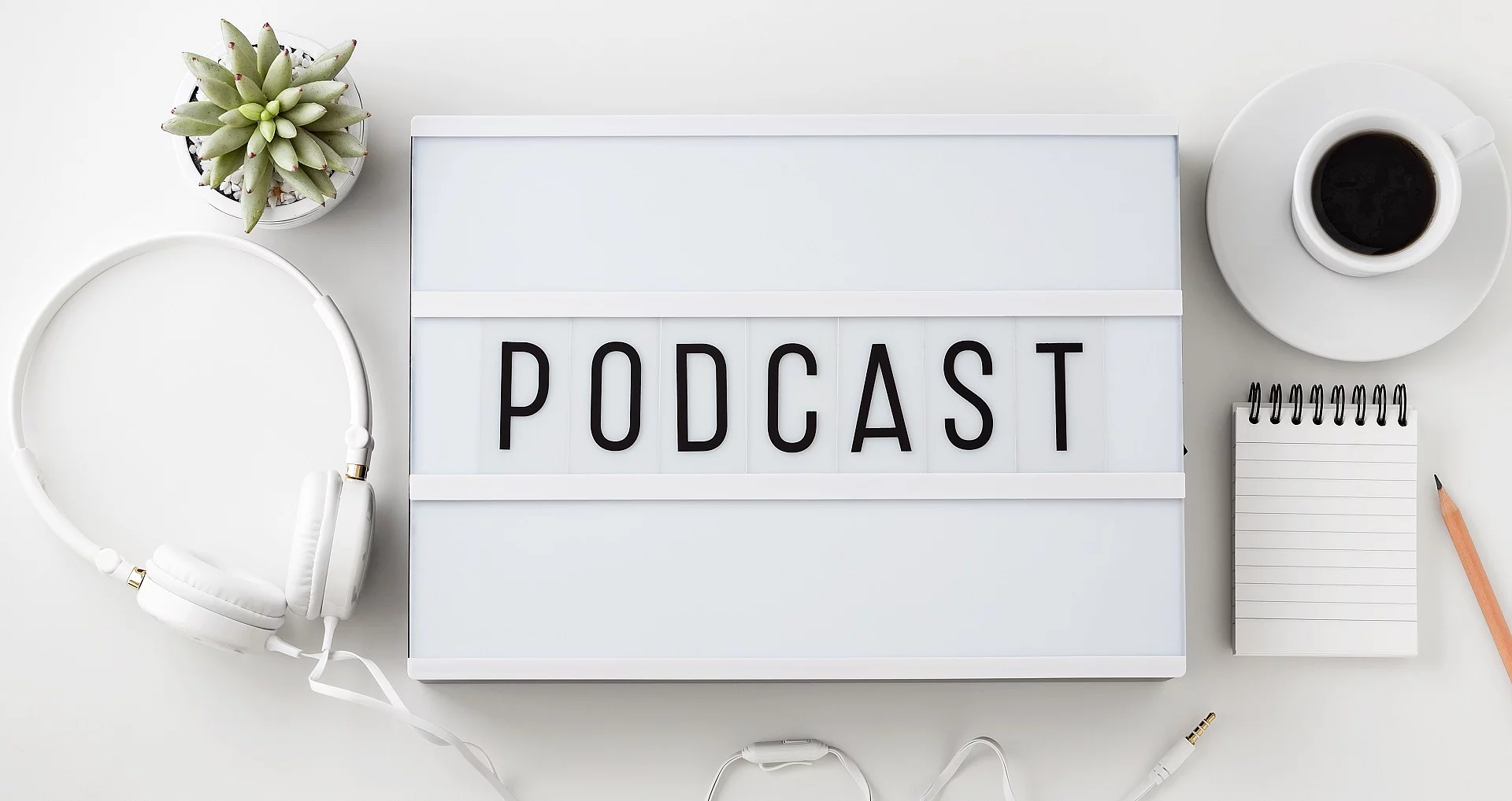 Weiße Box mit dem Schriftzug "Podcast". Daneben liegen Kopfhörer.