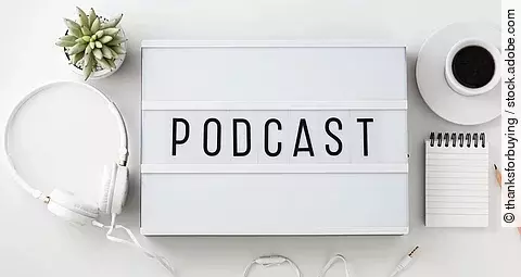 Weiße Box mit dem Schriftzug "Podcast". Daneben liegen Kopfhörer.