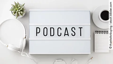 Weiße Box mit dem Schriftzug "Podcast". Daneben liegen Kopfhörer.