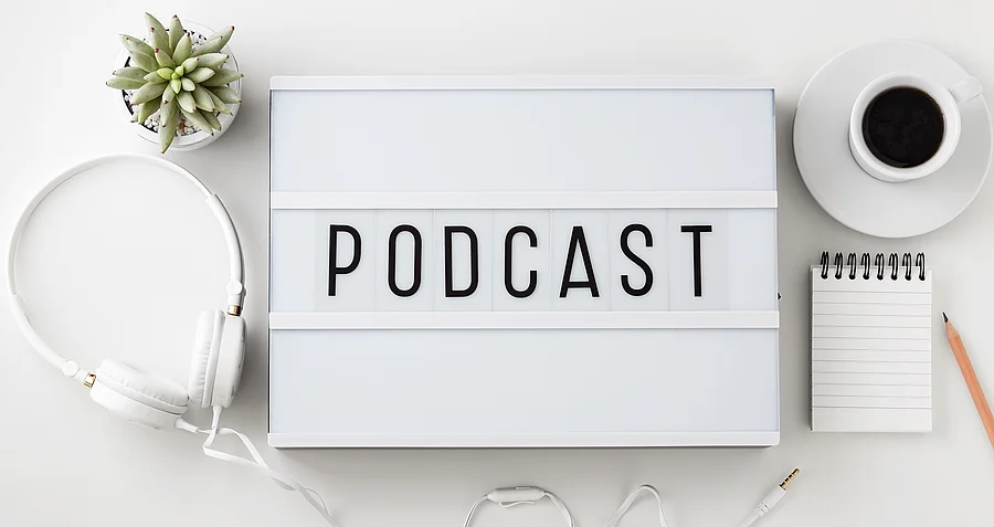 Weiße Box mit dem Schriftzug "Podcast". Daneben liegen Kopfhörer.
