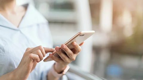 woman using smartphone on staircase in public areas, During leis Eine Frau nutzt ihr Smartphone. Die Person trägt eine Bluse. Das Handy ist ohne Hülle. Die Person trägt eine Armbanduhr. Der Hintergrund ist verschwommen.