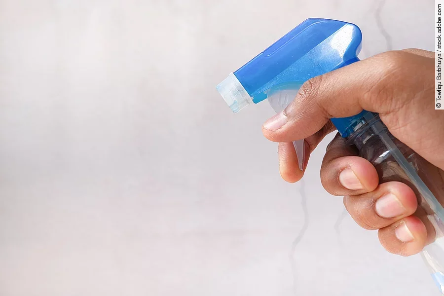 Nahaufnahme von einer Hand in der eine Sprühflasche gehalten wird.