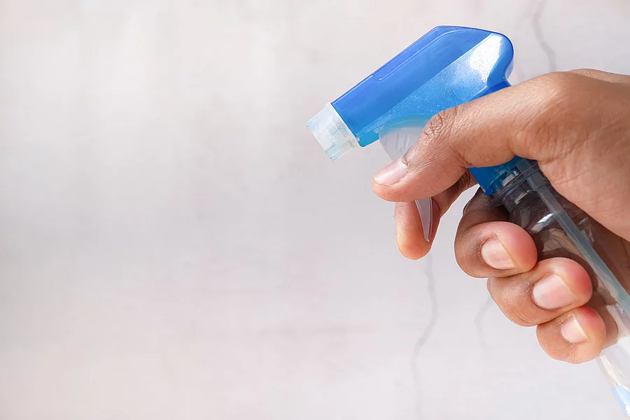 Nahaufnahme von einer Hand in der eine Sprühflasche gehalten wird.