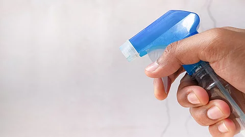 Nahaufnahme von einer Hand in der eine Sprühflasche gehalten wird.