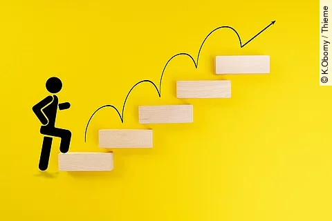 Ein schwarzes Ampelmännchen läuft eine Treppe hinauf. Die einzelnen Stufen bestehen aus braunen Holzbausteinen und liegen vor einem gelben Hintergrund. Ein schwarzes Ampelmännchen läuft eine Treppe hinauf. Die einzelnen Stufen bestehen aus braunen Holzbausteinen und liegen vor einem gelben Hintergrund.