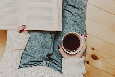 Eine Person hat ein aufgeschlagenes Buch und eine Tasse auf dem Schoß.