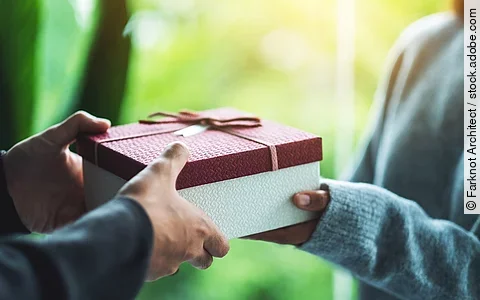 Nahaufnahme von einer Person die an eine andere Person ein Geschenk übergibt.