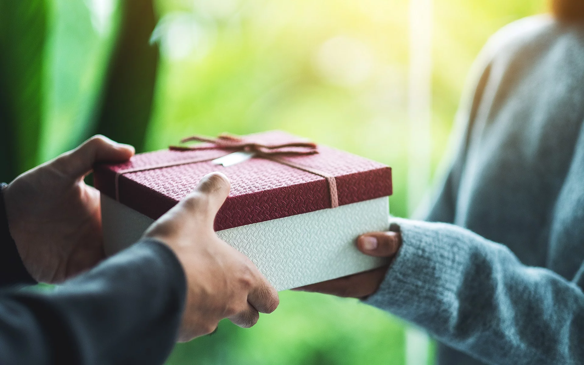 Nahaufnahme von einer Person die an eine andere Person ein Geschenk übergibt.