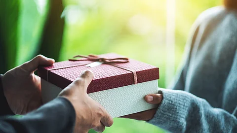 Nahaufnahme von einer Person die an eine andere Person ein Geschenk übergibt.